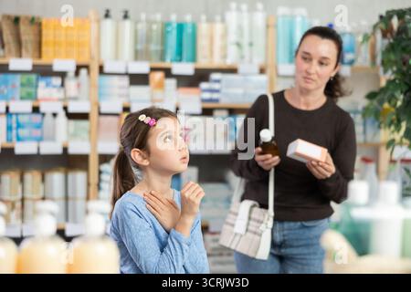 Das Kind steht und hustet in der Apotheke, und die Mutter wählt Medikamente Stockfoto