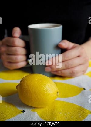 Frau, die Kaffeetasse mit natürlichen Nägeln und frischer Zitrone auf dem Tisch hält Stockfoto