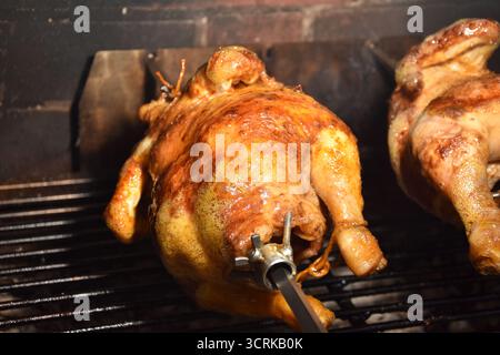 Ein Huhn, das auf einer Rotisserie gekocht wird. Rotisserie Chicken ist ein Gericht, bei dem ein ganzes Huhn auf einem Spieß aufgespießt und langsam über einer Wärmequelle geröstet wird Stockfoto
