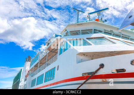 Von der Seite aus ist ein großes weißes Fährboot zu sehen, das das obere Deck und die Brücke vor dem blauen Himmel mit verstreuten weißen Wolken zeigt Stockfoto