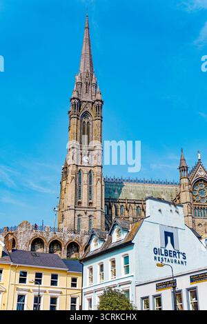 COBH, IRLAND - 15. August 2025: Die St. Colman's Cathedral erhebt sich über den farbenfrohen Geschäften und Pubs von Cobh und zieht Touristen an das bezaubernde Wasserfro der Stadt Stockfoto