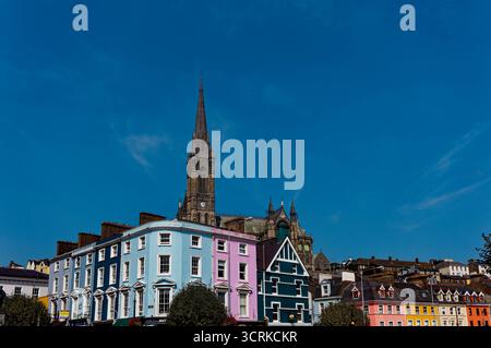 COBH, IRLAND - 15. August 2025: Die St. Colman's Cathedral erhebt sich über den farbenfrohen Geschäften und Pubs von Cobh und zieht Touristen an das bezaubernde Wasserfro der Stadt Stockfoto