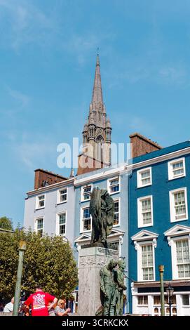 COBH, IRLAND - 15. August 2025: Die St. Colman's Cathedral erhebt sich über den farbenfrohen Geschäften und Pubs von Cobh und zieht Touristen an das bezaubernde Wasserfro der Stadt Stockfoto