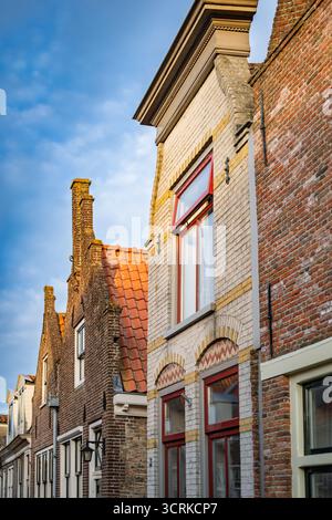 Eine bezaubernde Reihe traditioneller niederländischer Häuser mit Ziegelfassaden, Giebeldächern und rot gerahmten Fenstern unter einem hellblauen Himmel in Enkhuizen, Niederlande. Stockfoto