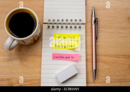 Leuchtende Haftnotizen mit englischem Text auf einem Notizbuch sowie Stift, Radiergummi und Kaffeetasse auf einem Holztisch – perfekt für Themen wie Planung und Tagebuch Stockfoto