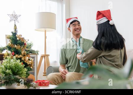 Die Weihnachtsfeier zeigt glückliches Paar, das zu Hause Liebe teilt, die Frau, die die Männerkrawatte anpasst, genießt Stockfoto