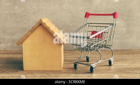 Miniatur-Einkaufswagen und Holzhausmodell für Kaufentscheidungen von Immobilien und Wohnungsmarkt Stockfoto