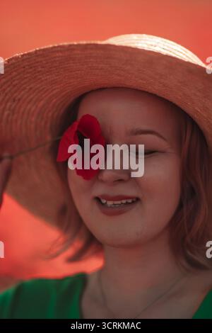 Mohn, Frau, Hut, der die Natur in einem leuchtenden roten Feld freudig umschließt Stockfoto