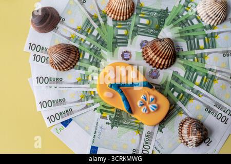 Stapel mit 100-Euro-Banknoten, die mit Flip-Flop und Muscheln auf Holztisch dekoriert sind. Konzept des Sommerurlaubsbudgets, Badeurlaubskosten, tra Stockfoto