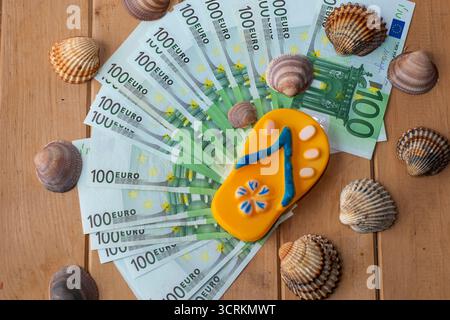 Stapel mit 100-Euro-Banknoten, die mit Flip-Flop und Muscheln auf Holztisch dekoriert sind. Konzept des Sommerurlaubsbudgets, Badeurlaubskosten, tra Stockfoto