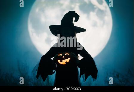 Mädchen in Hexenkostümen für Halloween. Junge, der auf Vollmond-Hintergrund steht. Stockfoto