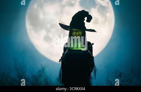 Mädchen in Hexenkostümen für Halloween. Junge, der auf Vollmond-Hintergrund steht. Stockfoto