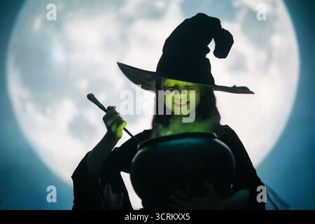 Mädchen in Hexenkostümen für Halloween. Junge, der auf Vollmond-Hintergrund steht. Stockfoto