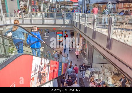 Geschäftige Shopping Mall Interior mit mehreren Etagen und Einkäufern auf Rolltreppen. Einzelhandelsflächen, Verbraucheraktivitäten, Handelszentrum, Geschäfte, Restaurants Stockfoto