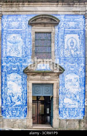 Die blau-weiße portugiesische Azulejos-Fliesenfassade umgibt den bogenförmigen Eingang und das Fenster einer historischen Kirche oder eines Gebäudes in Porto, Portugal Stockfoto