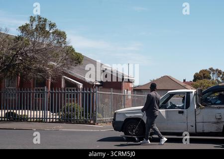 Ein netter afrikanischer Mann hilft einem älteren Mann beim Bewegen seines Pannenfahrzeugs (Bakkie), indem er das Vorderrad des in Schwierigkeiten geratenen Fahrzeugs auf einem Trolley hält. Stockfoto