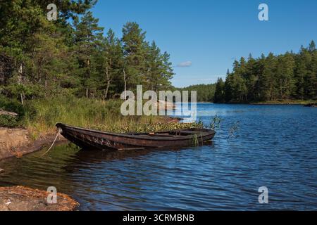 Rustikale schwedische Landschaft, Ruderboot auf blauem See umgeben von Nadelwäldern Stockfoto