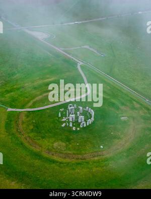 Aus der Vogelperspektive von Stonehenge, umgeben von Nebel, dessen alte Steine in starkem Kontrast zu den lebhaften grünen Feldern stehen, Salisbury, England, Vereinigtes Königreich. Stockfoto