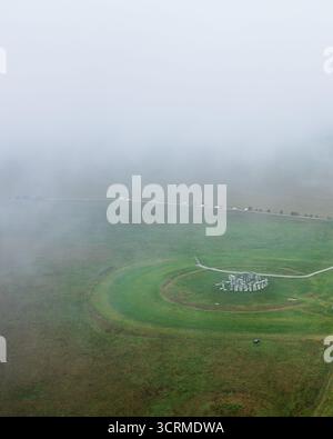 Aus der Vogelperspektive des alten Stonehenge Monuments, das in Nebel gehüllt ist, eine starke Silhouette vor den weitläufigen grünen Feldern, Salisbury, England, Großbritannien. Stockfoto