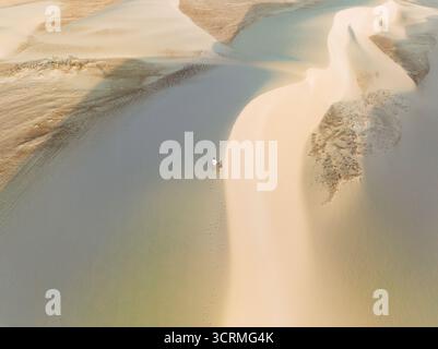 Aus der Vogelperspektive der sonnenverwöhnten Dünen werfen lange Schatten auf den welligen Sand, zwei winzige Figuren durchqueren die hügelige Landschaft, Socotra, Socotra, Jemen. Stockfoto