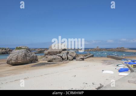 Am Hafenstrand von Tregastel auf der Cote de Granit Rose liegen kleine Boote bei Ebbe auf dem hellen Sand vor dem Hintergrund des berühmten rosa Stockfoto