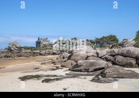 Blick vom Hafenstrand von Tregastel auf der Cote de Granit Rose bei Ebbe über die ikonischen rosa Granitfelsen zu einem typisch bretonischen Haus mit gr Stockfoto