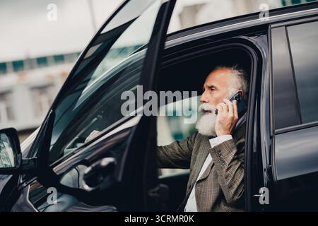 Selbstbewusster Geschäftsmann im Auto, der sich im Freien in urbaner Umgebung mit moderner Stadtkulisse unterhalten kann Stockfoto