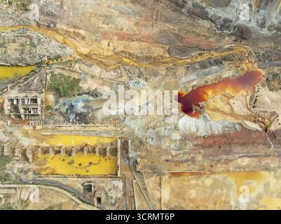 Aus der Vogelperspektive auf einen lebhaften, rostfarbenen Teich in der rauen, überirdischen Landschaft zeigt leuchtende Gelb- und Rosttöne inmitten der Überreste von Aband Stockfoto