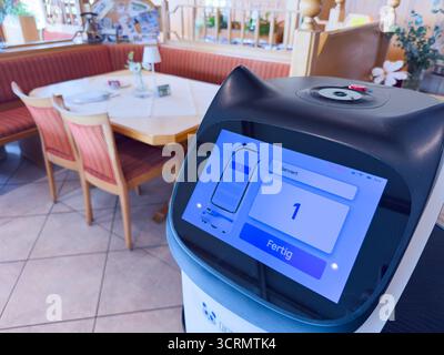 Heller Essbereich mit roten Polstersitzen und einem High-Tech-Food-Roboter mit Touchscreen-Display, der Gästen und Mitarbeitern am 1. September 2025 in Aitrang, Deutschland eine einladende, bequeme Café-Atmosphäre bietet. Stockfoto