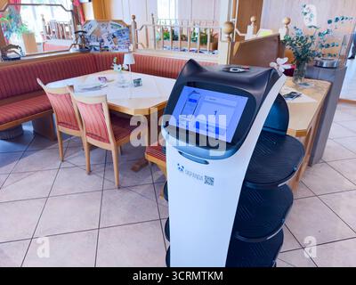Heller Essbereich mit roten Polstersitzen und einem High-Tech-Food-Roboter mit Touchscreen-Display, der Gästen und Mitarbeitern am 1. September 2025 in Aitrang, Deutschland eine einladende, bequeme Café-Atmosphäre bietet. Stockfoto