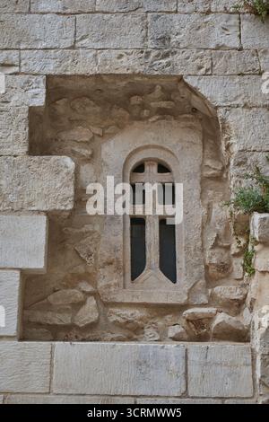 Nahaufnahme der mittelalterlichen Steinmauer mit Bogenfenster und geschnitztem Kreuz, Detail der historischen christlichen Architektur in Europa Stockfoto