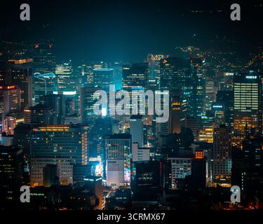 Nächtlicher Blick vom Namsan Tower über Myeongdong, Seoul, wo helle Stadtlichter aus dem geschäftigen Zentrum unter einem klaren, leuchtenden Himmel leuchten. Stockfoto