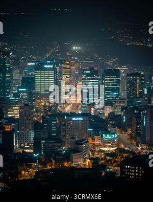 Nächtlicher Blick vom Namsan Tower über Myeongdong, Seoul, wo helle Stadtlichter aus dem geschäftigen Zentrum unter einem klaren, leuchtenden Himmel leuchten. Stockfoto