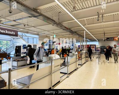 Salford, Großbritannien - 25. September 2025: Käufer nutzen Selbstkasse, während die Mitarbeiter an den Kassen in einem modernen, hellen Sainsbury's Geschäft helfen. Stockfoto