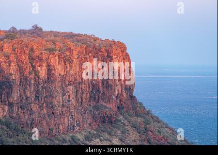 Rote Sandsteinklippen des Waterberg Plateaus, die im goldenen Sonnenuntergangslicht über den ruhigen Gewässern des Sees leuchten, Namibia, das südliche Afrika Stockfoto