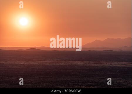 Feuriger goldener Sonnenuntergang über der dramatischen Erongo-Bergkette, glühende orange Sonne, die hinter Silhouetten von felsigen Bergrücken, die in warmes Dämmerlicht getaucht sind, in N Stockfoto
