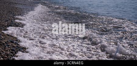 Weiche, schaumige Wellen Rollen an einem sonnigen, heißen Tag auf einem Kieselstrand Stockfoto