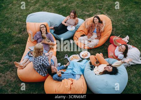 Freunde, die sich auf bunten Sitzsäcken im Freien entspannen und Essen und Getränke in zwangloser geselliger Atmosphäre mit einem kleinen Hund teilen. Frau informell Stockfoto