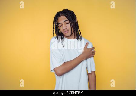 Porträt eines jungen Mannes mit stilvollen Dreadlocks posiert nachdenklich und reflektiert eine ruhige Stimmung auf gelbem Hintergrund Stockfoto