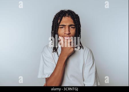 Porträt eines jungen Mannes mit einem nachdenklichen Ausdruck, der sein Kinn auf seiner Hand auflegt, was auf einen hellen Hintergrund hinweist Stockfoto