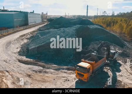 Ein Bagger gießt Ton in einen Müllwagen zur Ziegelherstellung. Stockfoto