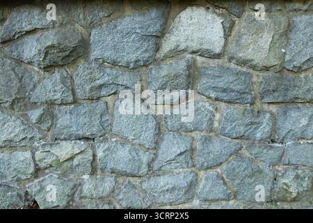 Steinmauer mit unregelmäßigen grauen Felsen, rustikale Hintergrundtextur der Mauerwerkkonstruktion Stockfoto