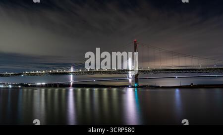 Queensferry Crossing, eine moderne, mit Kabel überspannende Brücke über Firth of Forth, die nachts hell beleuchtet wird und ihre Lichter auf dem stillen Wasser reflektiert Stockfoto