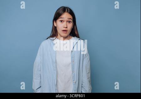 Eine überraschte junge Frau in einem gestreiften Hemd auf blauem Hintergrund. Stockfoto
