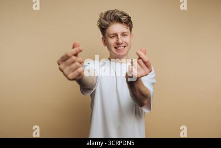 Ein junger Mann steht vor einem neutralen Hintergrund, lächelt hell und streckt die Arme nach vorne. Er greift in spielerische Handgesten ein, die Frien transportieren Stockfoto