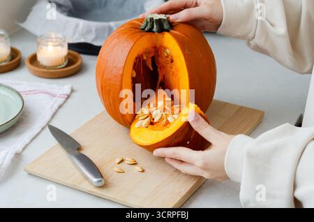 Frau, die geschnittenes Stück frischen Bio-Kürbis mit Samen zum Herbstkochen hält Stockfoto