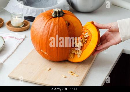 Frau, die geschnittenes Stück frischen Bio-Kürbis mit Samen zum Herbstkochen hält Stockfoto