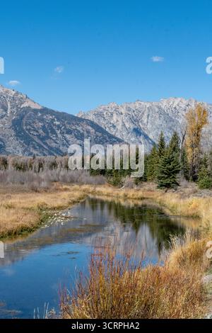 Schneebedeckte Gipfel der Grand Teton Mountain Range stehen vor einem klaren blauen Himmel mit ihren Reflexen im Snake River Stockfoto