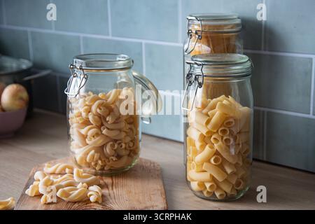 Verschiedene Formen von ungekochten Nudeln, die in traditionellen luftdichten Glasbehältern wunderbar aufbewahrt werden. Die Komposition hebt die verschiedenen Texturen hervor Stockfoto