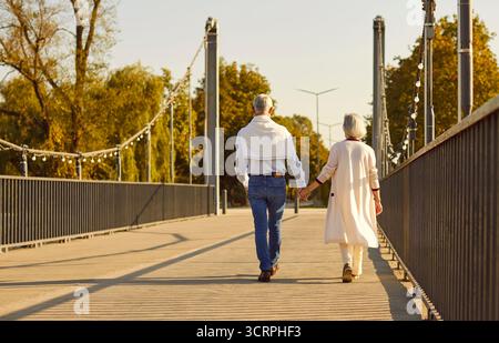 Seniorenpaar, das Hand in Hand auf der Brücke an sonnigen Herbsttagen im Freien spaziert Stockfoto